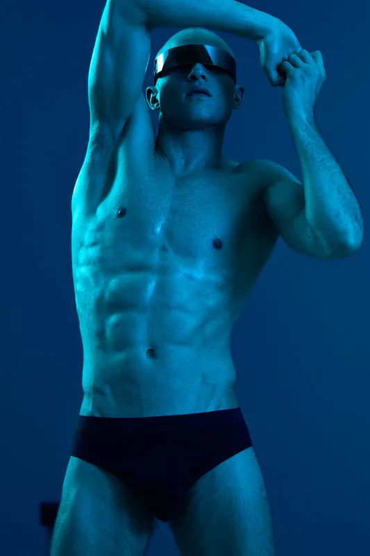 Stylish man posing in a blue light, showcasing his muscular physique. The striking contrasts emphasize the details in this captivating black and white image.