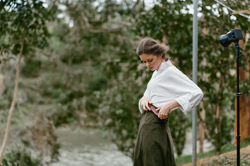 Elegantly dressed model adjusting her outfit in a serene outdoor setting, showcasing natural beauty and confidence amidst lush greenery and soft sunlight