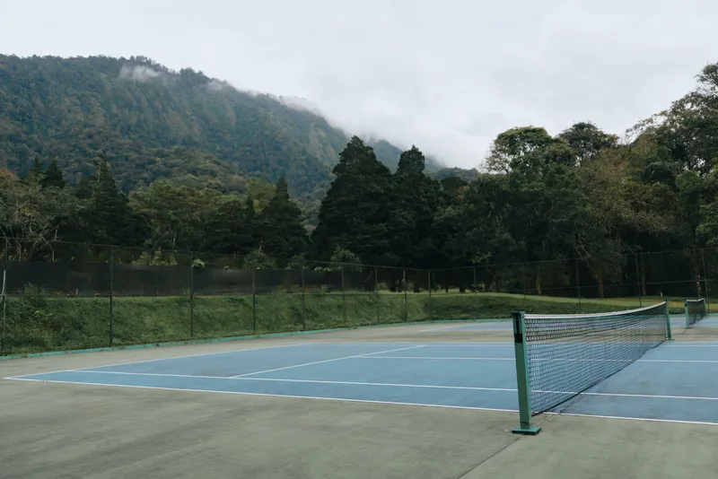 Empty tennis court surrounded by lush greenery and misty mountains, perfect for serene sports photography in a tranquil environment