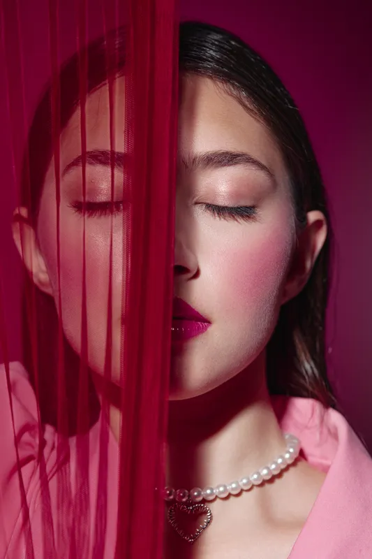 Creative beauty portrait of young woman with closed eyes and pink makeup behind red fabric. Concept for fashion, cosmetics, elegance, and sensuality in art photography.
