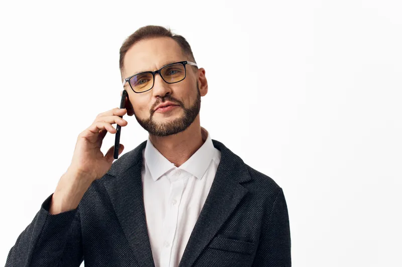 A professional businessman on an isolated colored background, speaking on a mobile phone with calm confidence. He wears a dark blazer and white shirt, and the pose conveys readiness, focus, and