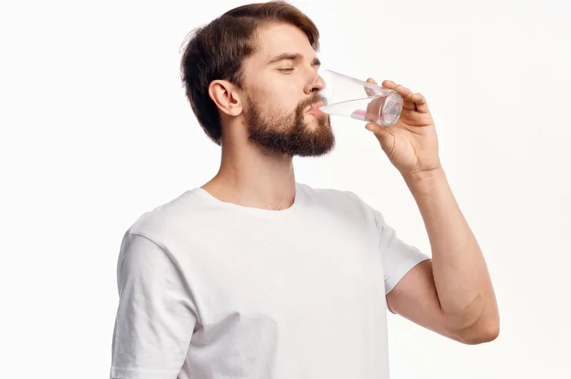 Симпатичный парень со стаканом воды на белом фоне, футболка, кадрированный вид