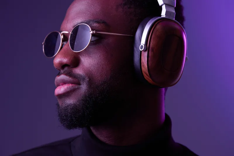 Fashionable Black man wearing stylish headphones and sunglasses, conveying confidence and style against a purple background