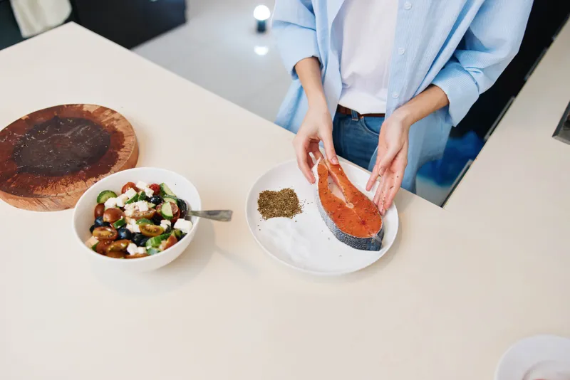 Женщина держит тарелку с рыбой и миску с едой на столе