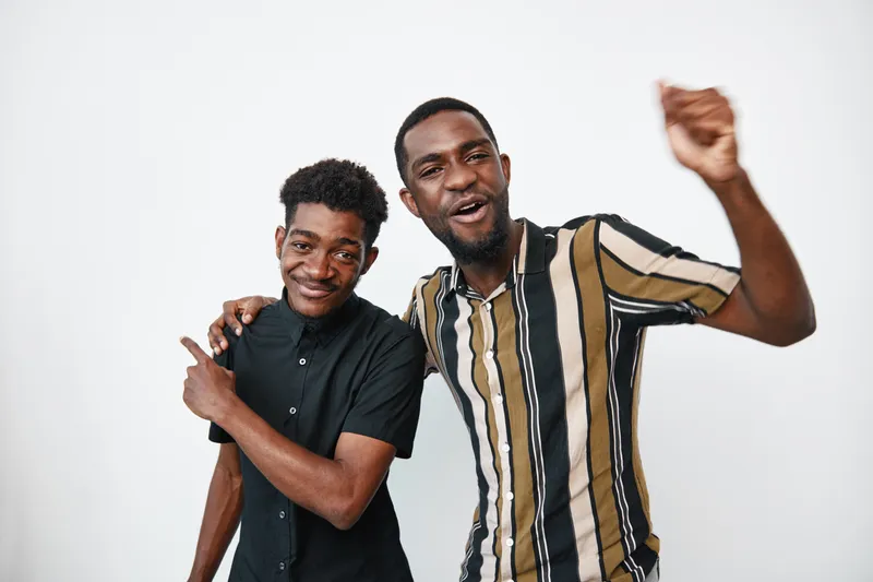 Two African American men with dark skin smiling and posing together in casual clothing on white background. Friends, happiness, and joyful expression in studio portrait.