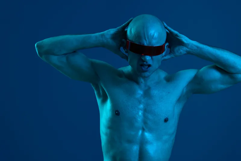 Athletic man striking a bold pose against a blue background, showcasing confidence and strength, emphasizing a dramatic and modern style in a captivating visual.
