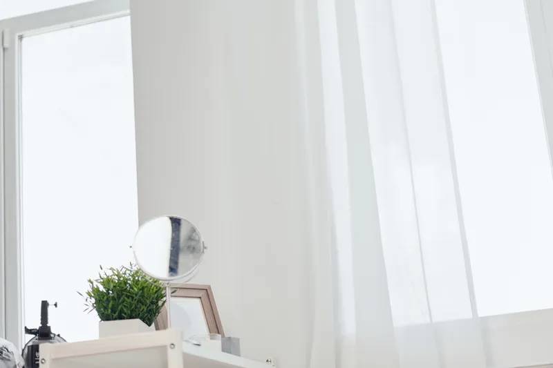 A cozy modern room with a young woman sitting by the window, surrounded by natural light and minimalist decor, creating a serene atmosphere perfect for relaxation.