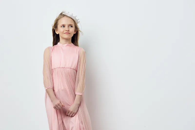 Elegant young girl with long hair in a pink dress and flower crown, exuding a sense of innocence and beauty against a minimalist white background