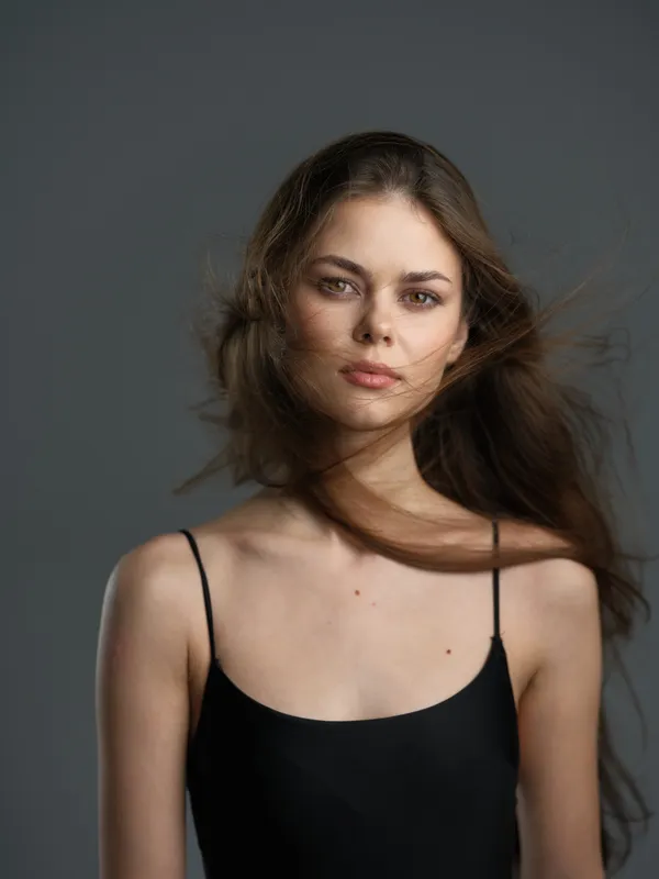 young woman with flowing hair wearing black top with thin straps against gray background