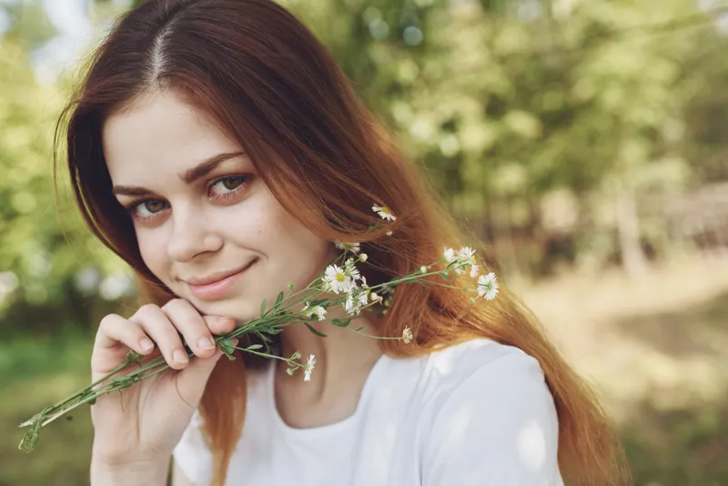 Симпатичная женщина с белыми полевыми цветами стоит в поле возле деревьев