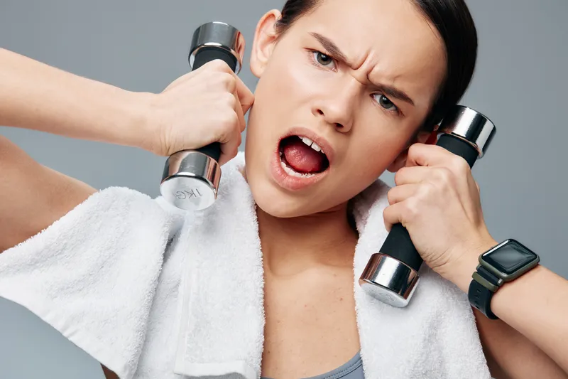 Female athlete with towel and dumbbells performing an intense workout that captures fitness, sport spirit, strength and focus during a high energy training moment.
