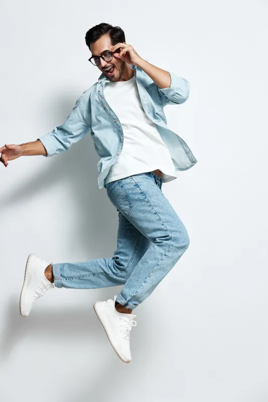 Full body joyful smiling young man wearing casual outfit jumping with excitement in the air while looking at the camera on solid light background. People lifestyle concept.