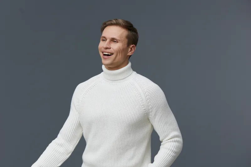 Bright smiling cheerful man in white sweater looking away isolated on plain gray background studio portrait. People lifestyle concept adult male happiness joy clothing casual fashion