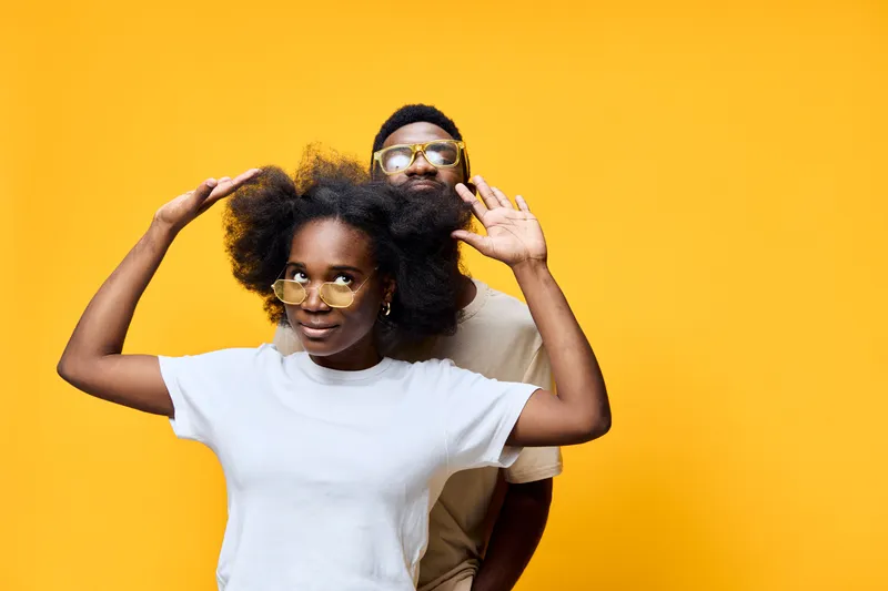 Joyful African American couple enjoying playful moments against a vibrant yellow background, showcasing stylish fashion and cheerful emotions