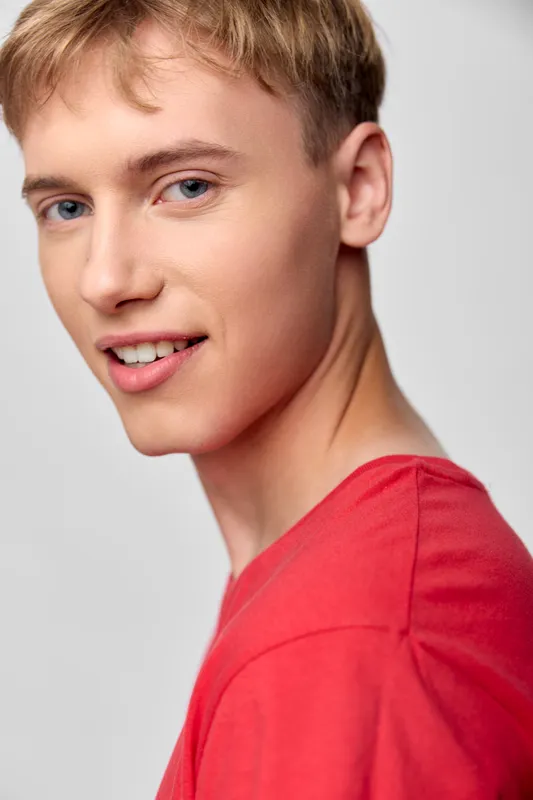 Smiling young man in a red shirt with casual style for fashion, lifestyle or head and shoulders studio shot, warm lighting, clean background, expressive mood, approachable vibe, contemporary model.