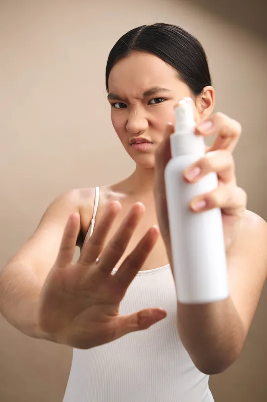 asian woman in a clean indoor setting uses a spray bottle with a calm, focused expression, conveying hygiene and care as she treats a surface.
