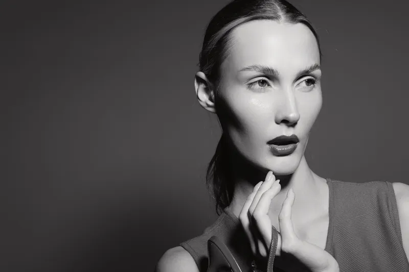 Portrait of a slender Caucasian woman with pale skin and slicked back hair in studio black and white light.