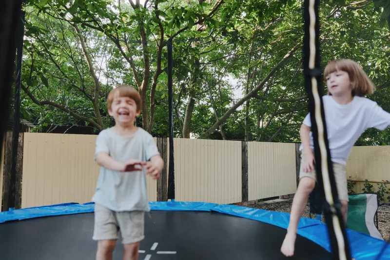 Happy children jumping on a trampoline in a sunny backyard, enjoying playful moments with joy and excitement. Perfect for family lifestyle themes and outdoor fun.