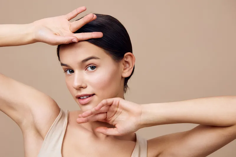 Young woman with smooth skin showing playful emotions against a soft beige background, ideal for beauty and skincare concepts