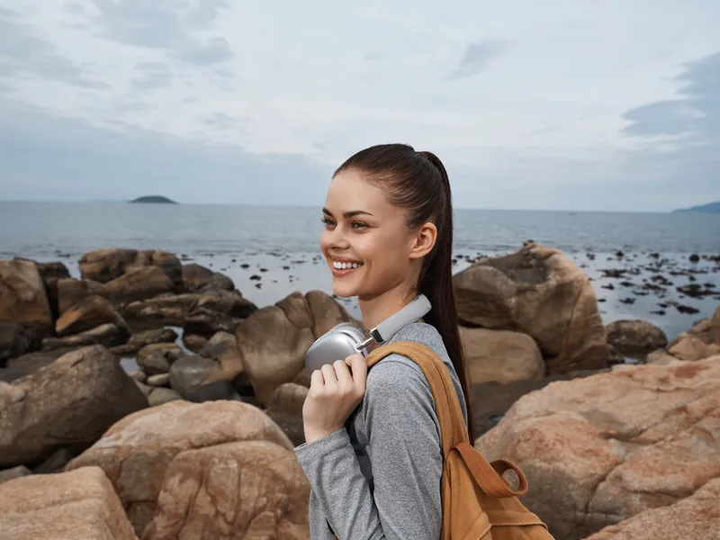 Happy young woman with backpack holding a water bottle by the rocky beach, promoting eco friendly lifestyle and outdoor adventure