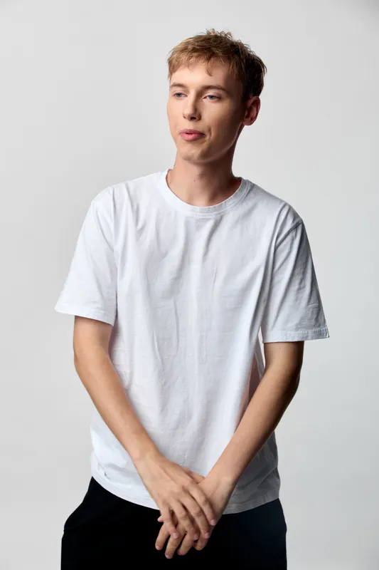 Man in a white t shirt stands in a simple studio setup with a relaxed pose and thoughtful expression, conveying casual confidence and modern minimalism for stock imagery