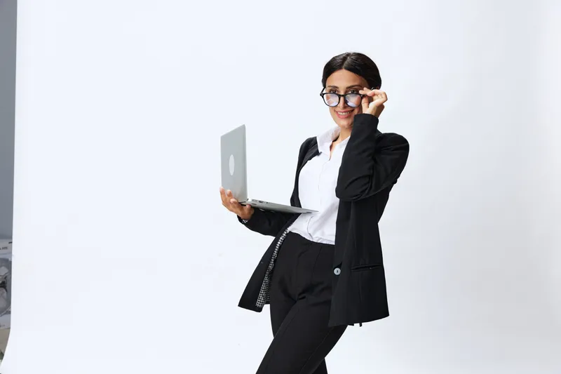 Деловая женщина с ноутбуком в руках, в черном деловом костюме, показывает жесты и эмоции на белом фоне