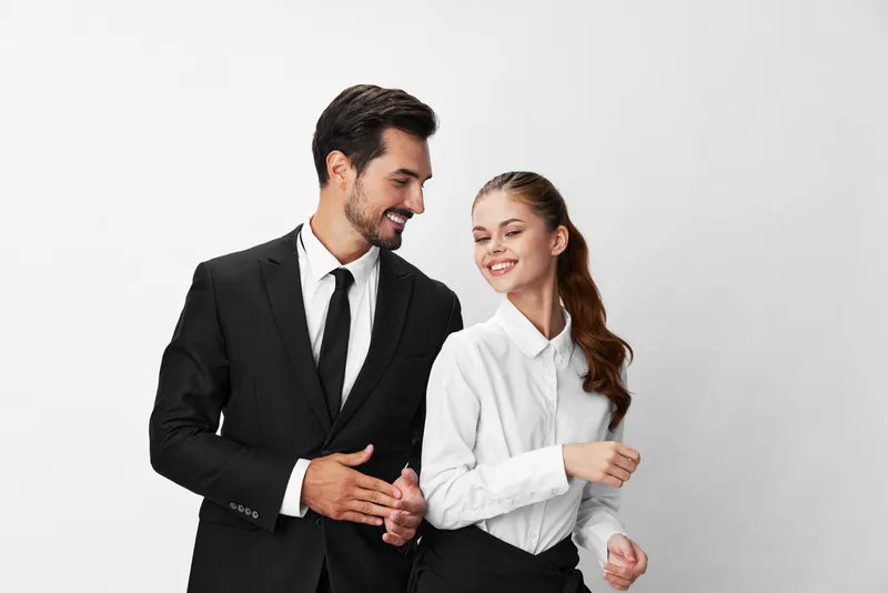 Мужчина и женщина улыбаются, показывая зубы, одетые в деловые костюмы, и смотрят в камеру на белом изолированном фоне