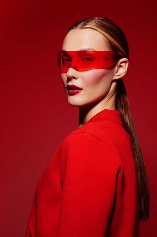 Portrait of a stylish woman wearing red futuristic glasses and a red outfit against a red background. Concept of fashion, modern style, and bold color contrast.