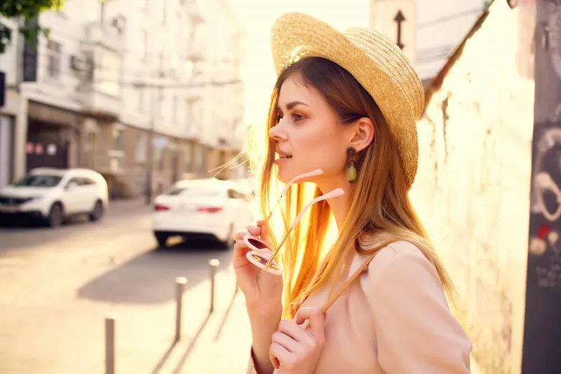 На улице стоит красивая женщина в шляпе и очках