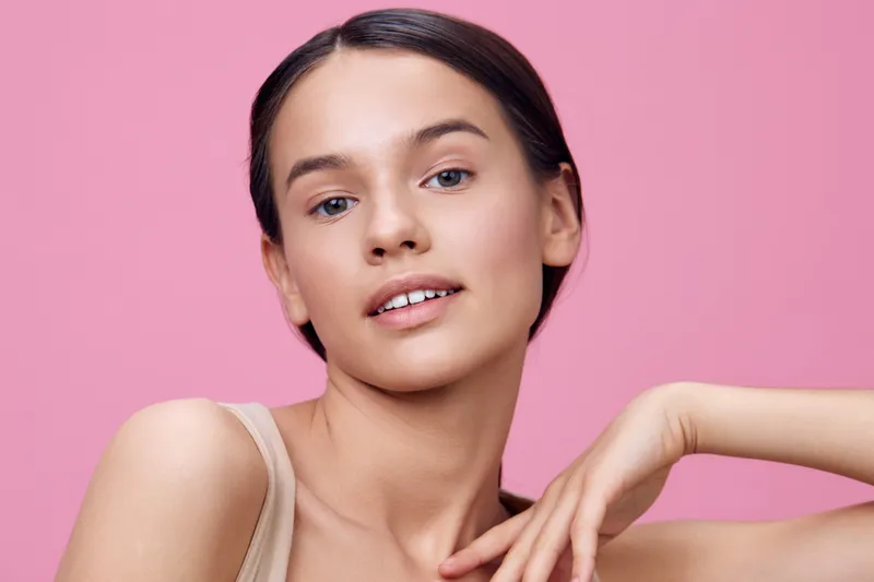 Young woman with natural makeup poses confidently against a soft pink background, showcasing beauty and self expression Perfect for health and wellness themes