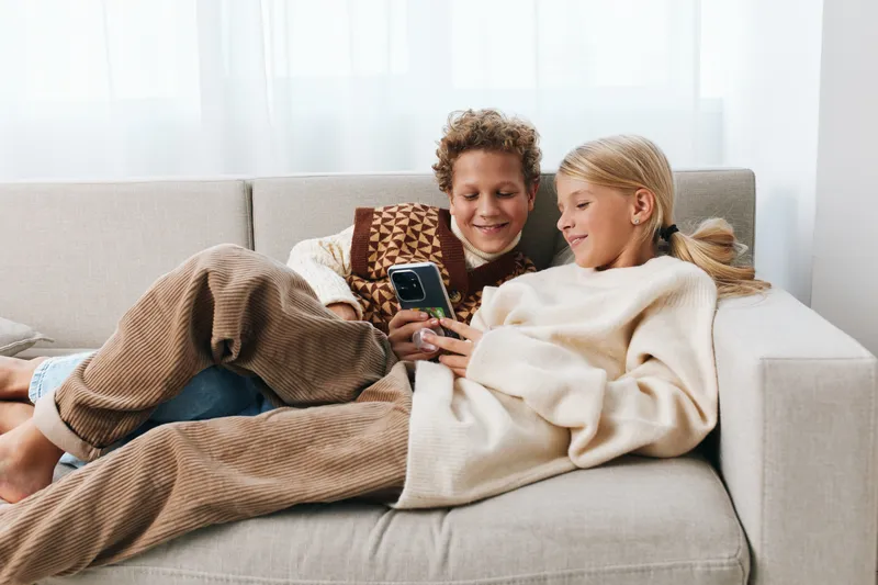 Authentic moment of friends enjoying a playful game on a smartphone at home, blending school charm with a relaxed lifestyle and cozy, candid atmosphere.