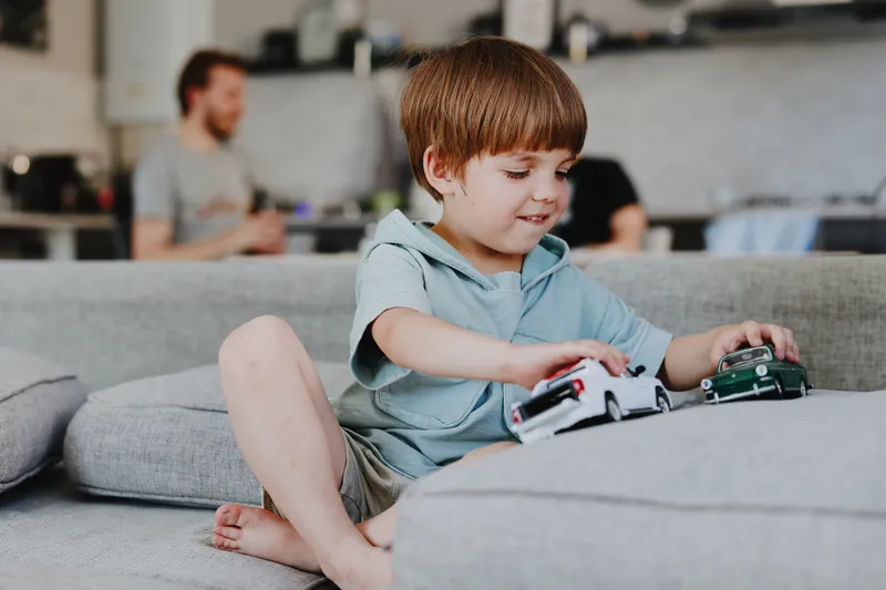 Happy boy playing with toy cars at home, showcasing creativity and imagination while engaging in joyful playtime with family members in the background.