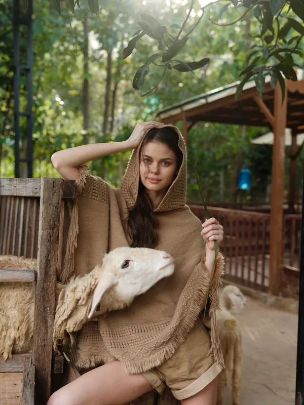 Женщина в коричневой шали сидит на деревянной скамейке рядом с овцой