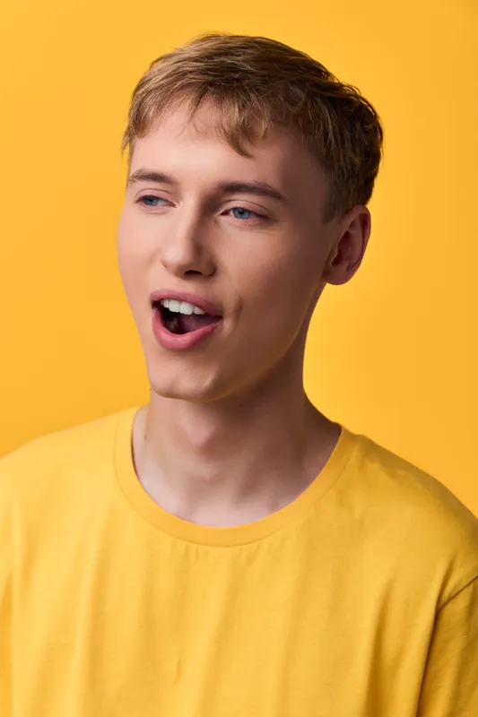 Surprised, young man in a yellow shirt in studio lighting, capturing a vivid moment of astonishment and casual charm, ideal for lifestyle, fashion or playful advertising campaigns