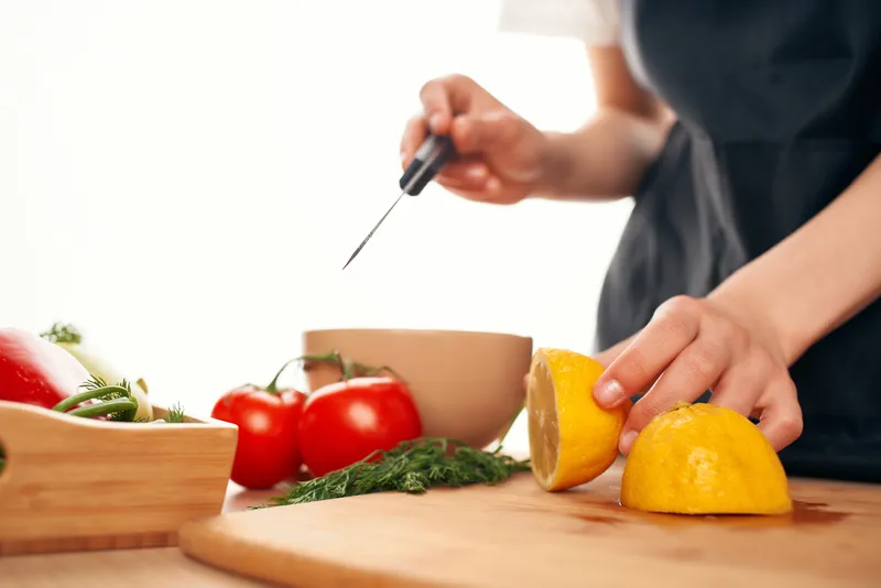 Шеф-повар с ножом в руках нарезает овощи и лимон на кухне, домашняя готовка