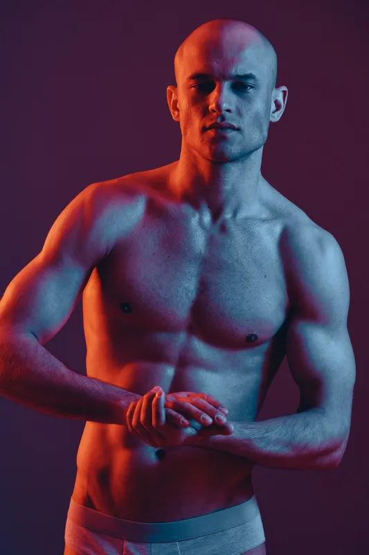 Strong man posing confidently in dramatic lighting, showcasing athletic physique and bold presence, emphasizing strength and vitality in a colorful portrait.