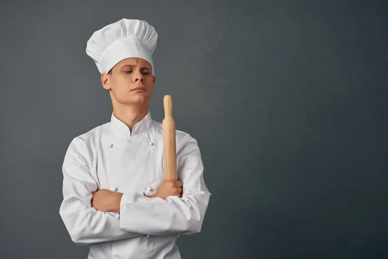 Весёлый шеф-повар в униформе, предметы кухни в руках профессионала ресторана