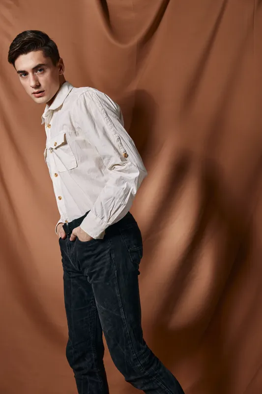 Мужчина в белой рубашке держит руки в карманах, излучая уверенность в себе и современный стиль