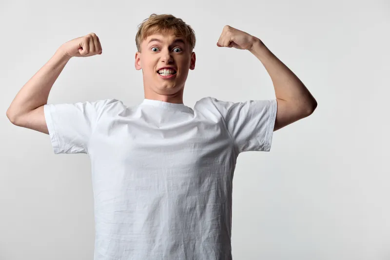 Excited man in a white t shirt flexing arms, showcasing energy and confidence in a clean studio setting. Dynamic pose, positive vibe, casual style, and confident expression conveying motivation and