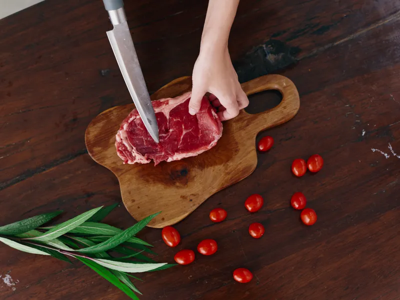 Женщина с ножом в руке нарезает свежее стейковое мясо для жарки на кухне