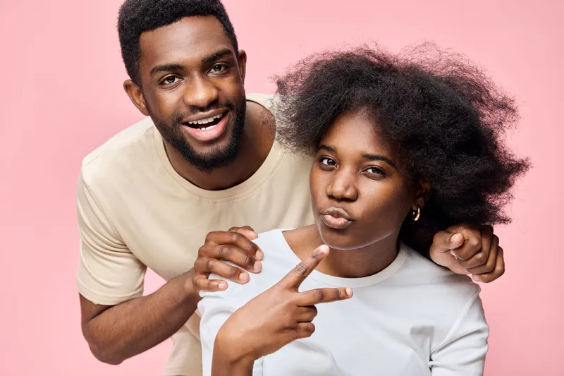 Happy couple showcasing playful emotions on a soft pink background, wearing casual light colored outfits Key themes include joy, togetherness, and modern lifestyle