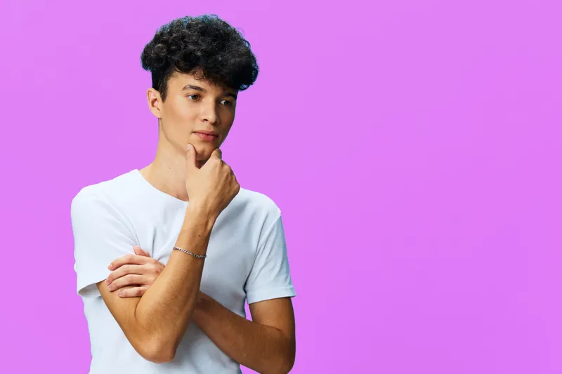 thoughtful young man with curly hair wearing white t-shirt, posing against bright purple background with contemplative expression, casual style, studio lighting
