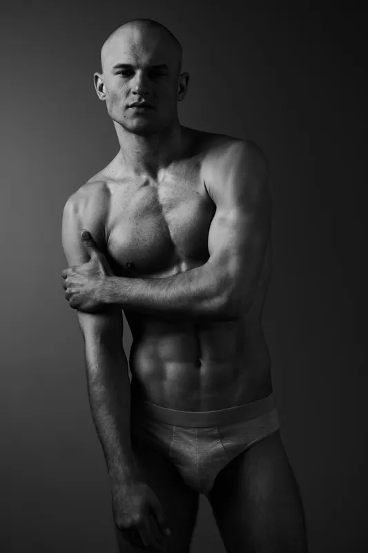 Black and white portrait of a confident man showcasing strong physique and expressive stance, highlighting masculinity and artistic character.