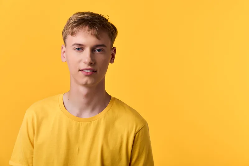 Young man in a yellow shirt stands before a yellow background front view studio shot head and shoulders casual minimal composition with bold color and neutral lighting for modern approachable style