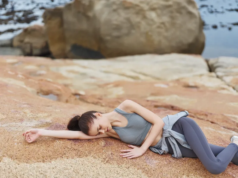 A serene fitness model in athletic wear relaxing on a rocky beach, embodying calmness and tranquility with a focus on health and wellness