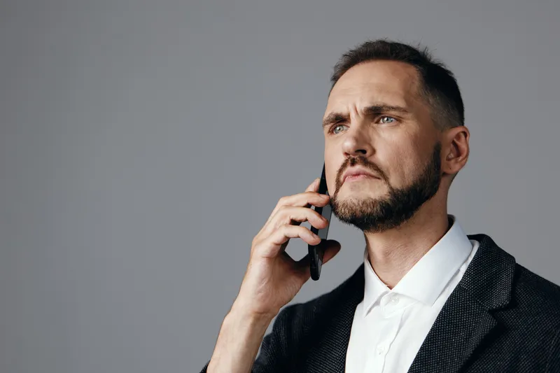 A focused business professional on a call, isolated against a gray background, exudes calm confidence and determination while discussing strategic matters and pressing decisions.
