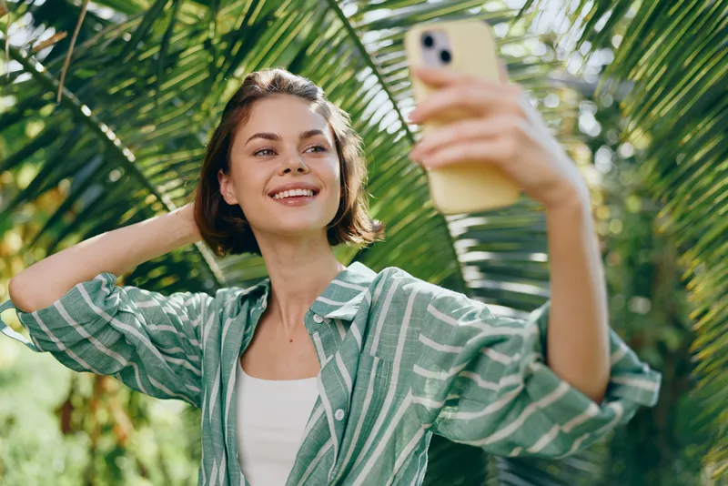 Woman, selfie, outdoors, smile a cheerful woman takes a selfie in bright daylight, standing among lush greenery, relaxed pose, casual outfit, radiating confidence and joy
