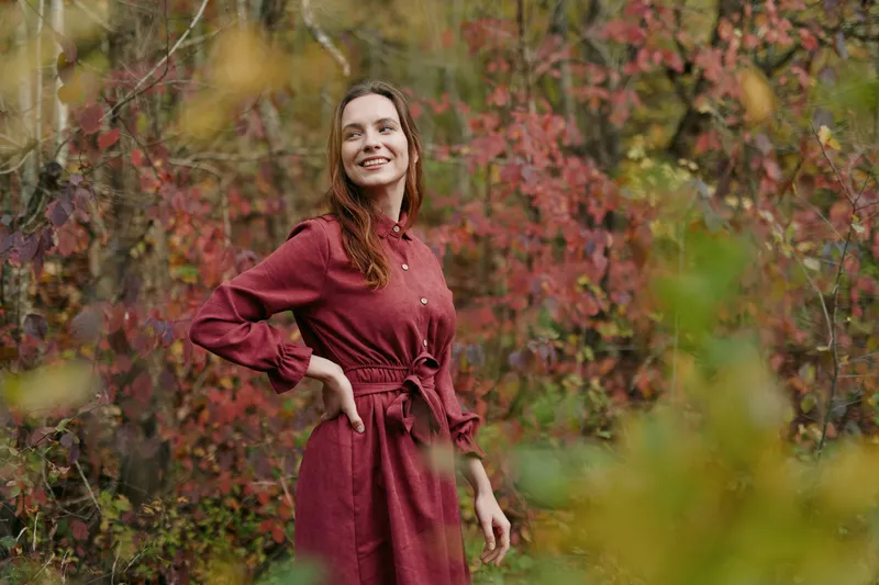 A candid portrait of a woman in a red dress among autumn foliage, capturing a genuine, authentic mood with a natural pose and expression, soft natural light and warm tones conveying credibility and