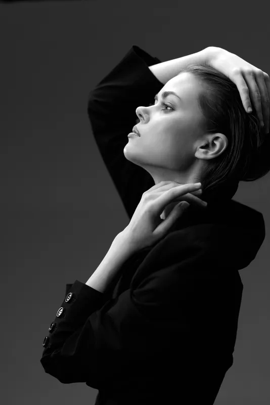 Black and white portrait of a thoughtful woman in a dark jacket with a dramatic pose and smooth lighting.