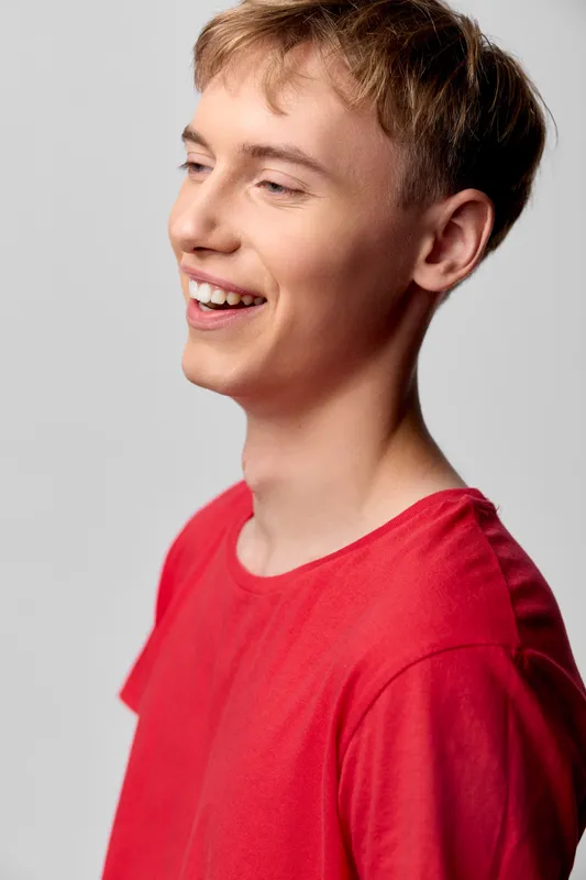 Smiling young man in a red shirt conveys happiness and confidence in a bright studio, highlighting a relaxed expression and positive mood for lifestyle, fashion, and casual studio imagery